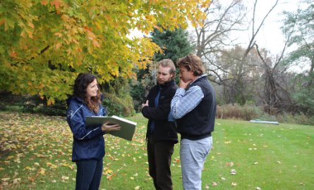 3 Staff members standing in open grassy area and reviewing information in binder